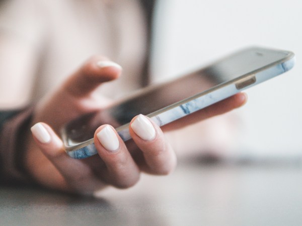 A person wearing white nail polish while using their phone with one hand.