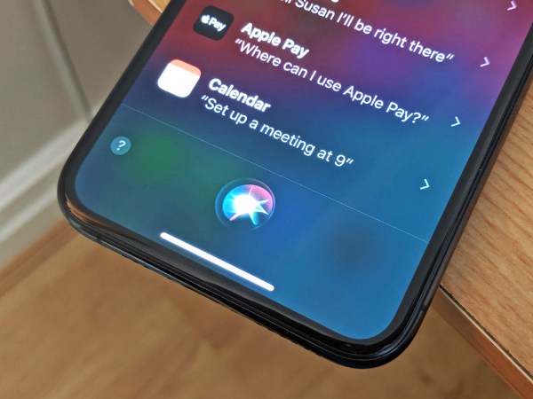 An iPhone on a wooden table showing Siri on its screen.