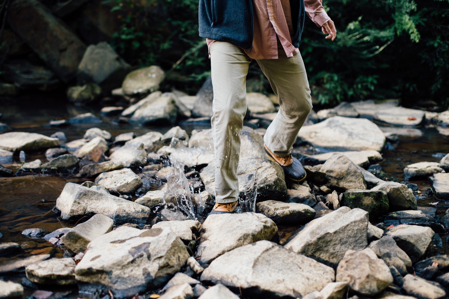 a person crossing a rocky stream while wearing long pants and boots