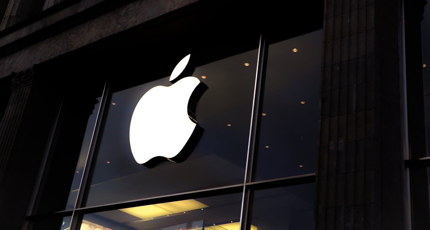 A white Apple logo on the black paneling in front of an Apple store.