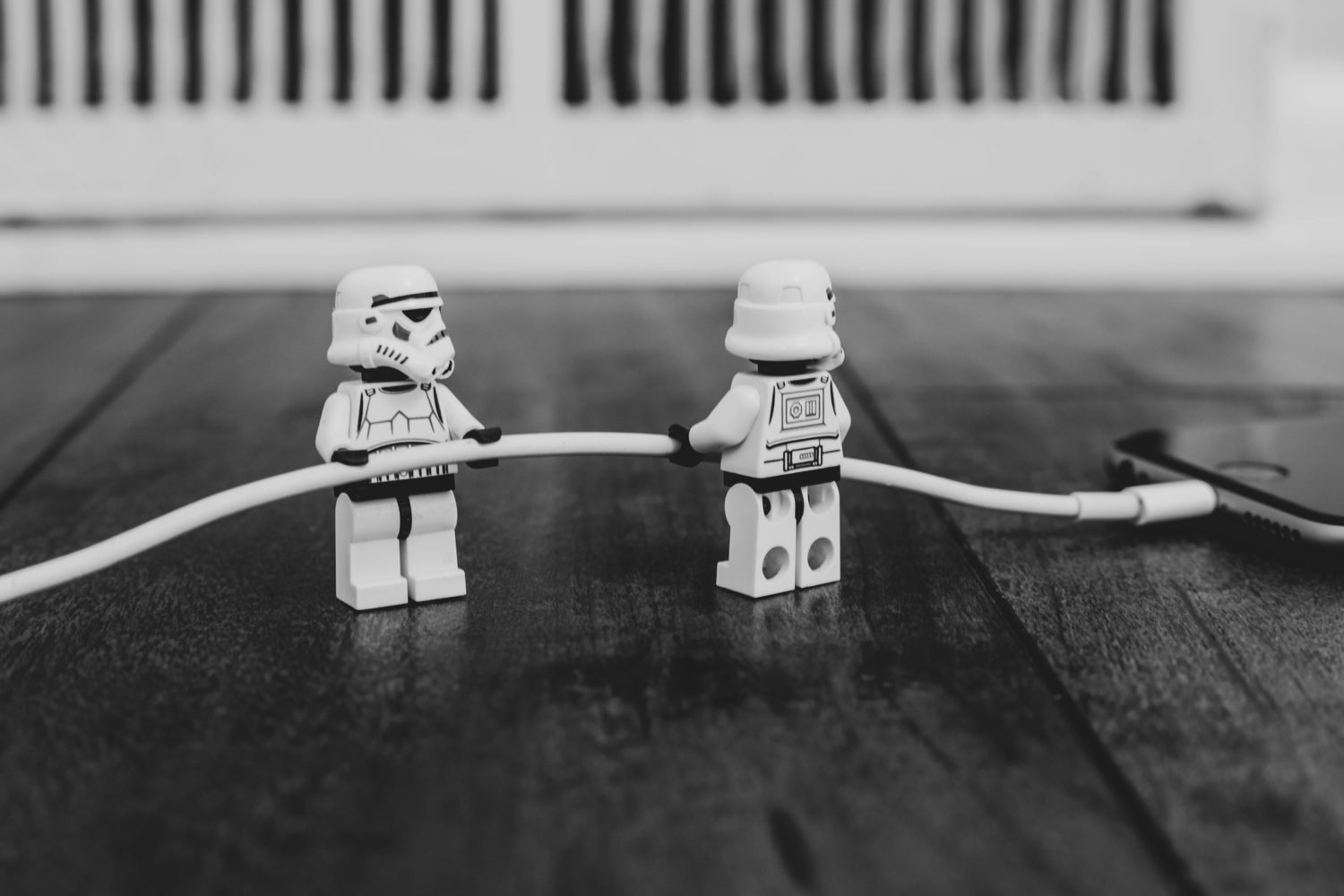 Stormtrooper Lego figurines holding an iPhone cable that's connected to an iPhone laying on a black wooden surface.