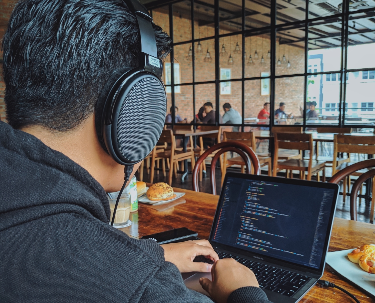 A man working on a laptop in a coffee house with headphones on.