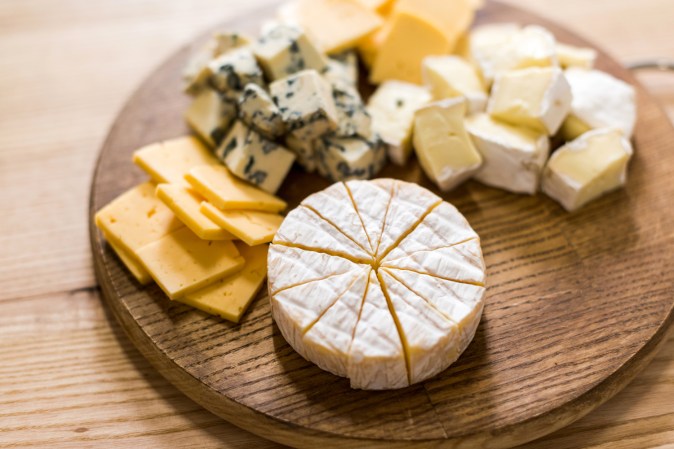 a cheese board with different cheeses of different shapes