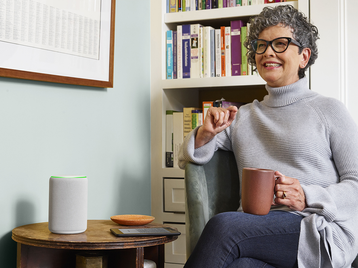 Person holding a cup of tea sitting next to a table with an amazon echo on it