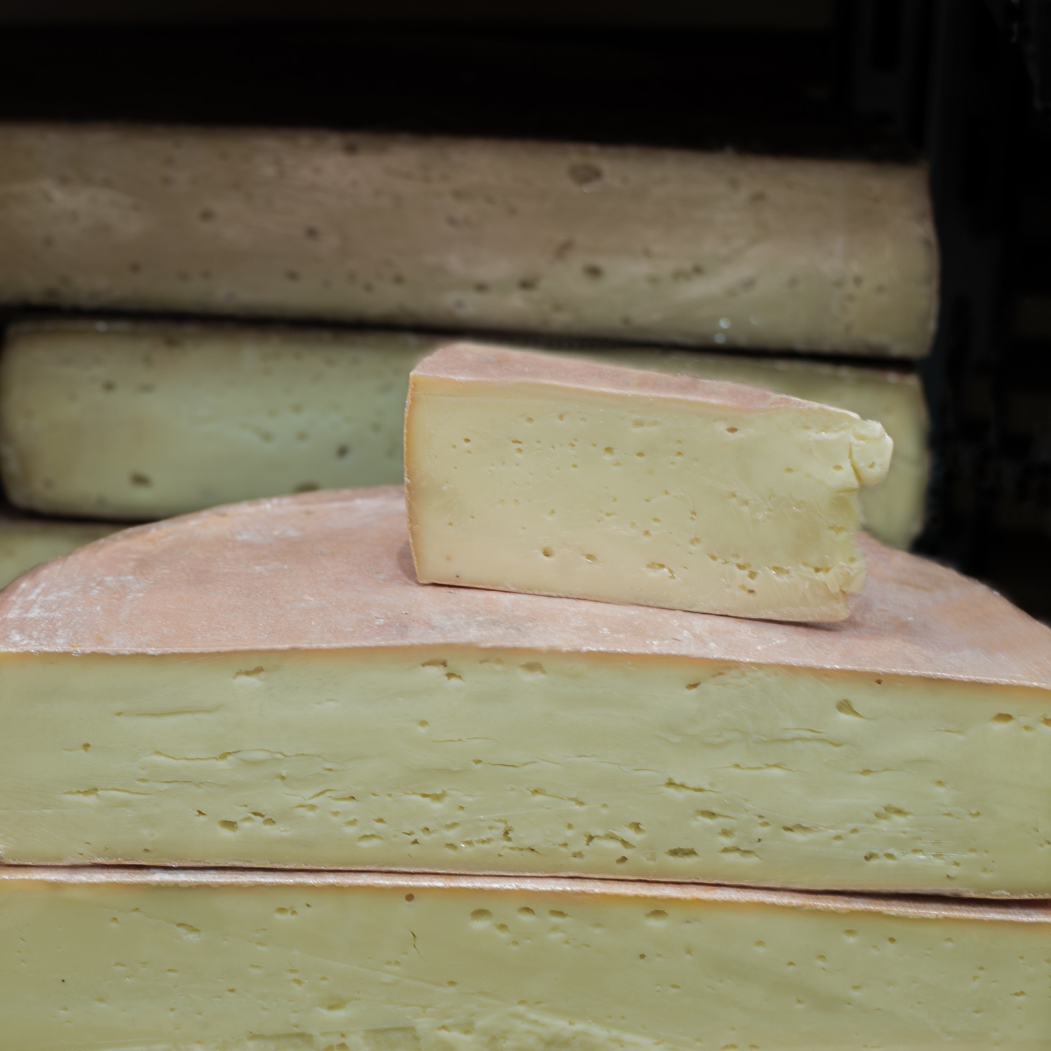 a wedge of soft cheese sitting on top of two halves of a wheel of cheese in a cheese display