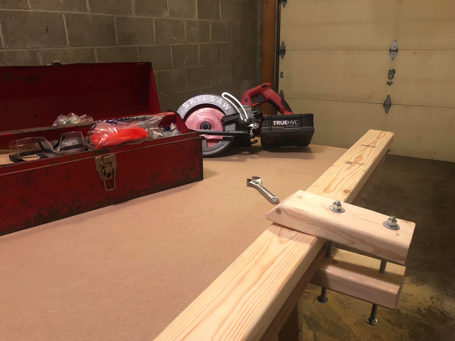 a basic wooden clamp holding a 2-by-4 stud down on a work surface in a garage