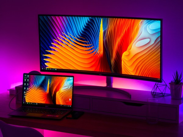 A laptop computer set up with two screens and backlit by a purple LED light.