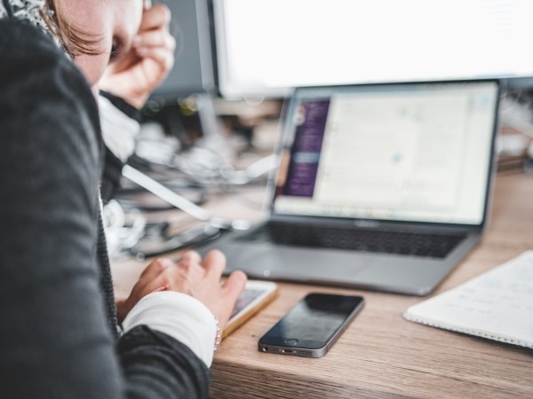 A person leaning over a desk working on two phones and a laptop, as one might do when it’s time to switch phones.