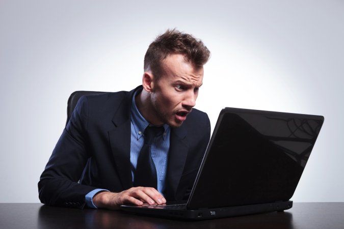 Man sitting at his laptop and looking surprised while reading something.