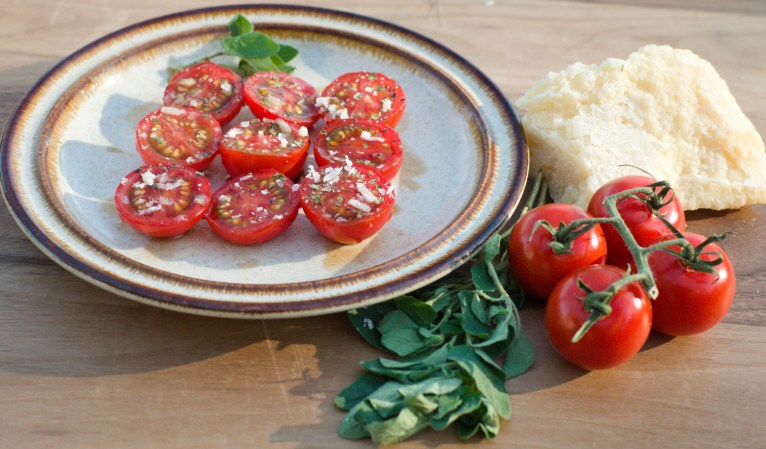 halved cherry tomatoes on a plate with marjoram, parmesan cheese, and other spices