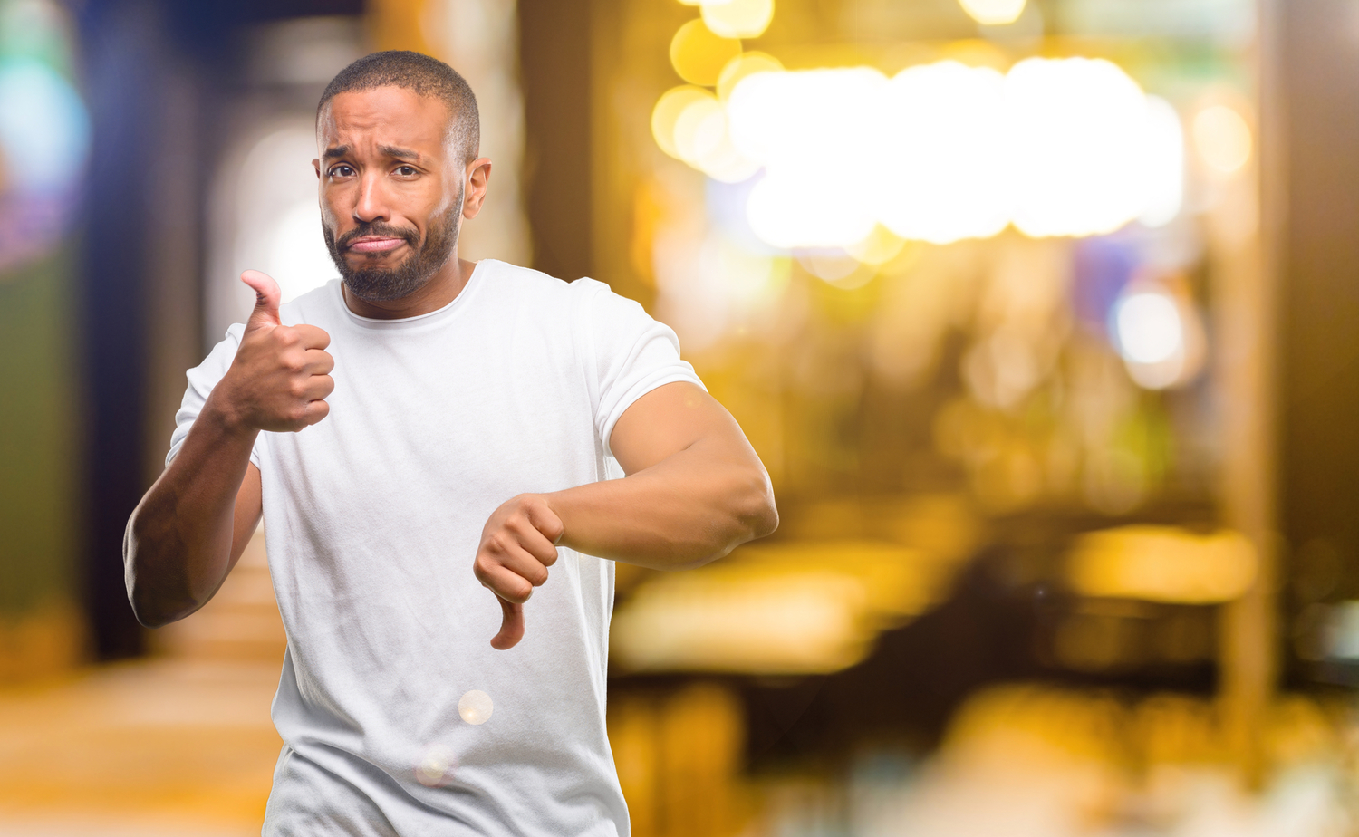 a black man giving a thumb's up and thumb's down sign while looking confused and standing near some lights at night