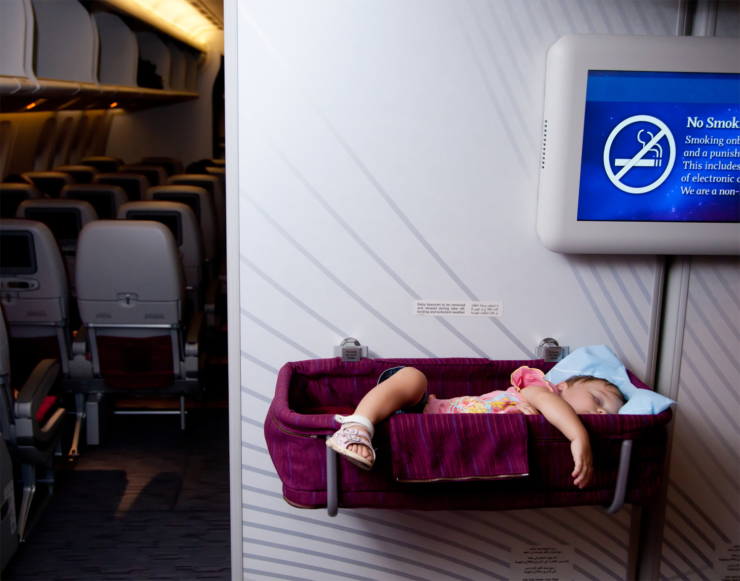 Small two year old baby girl sleep in a special bassinet on a airplane