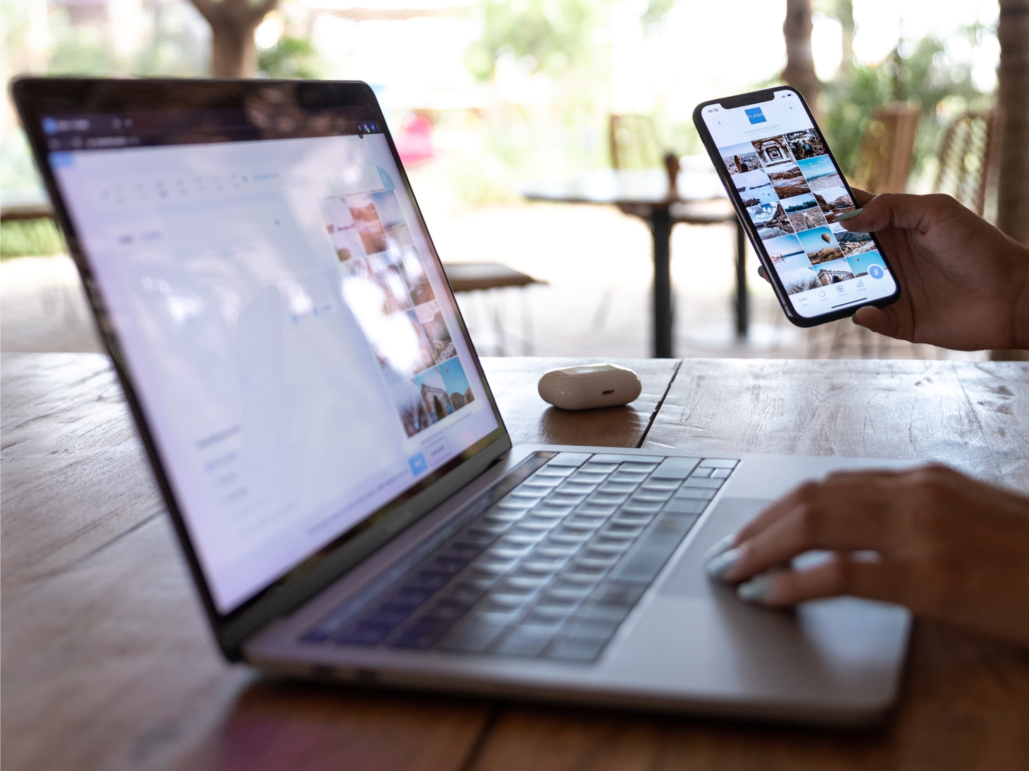 A person using a phone and a laptop while sitting at a wooden table.