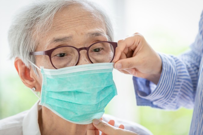 someone helps an older woman put on a face mask