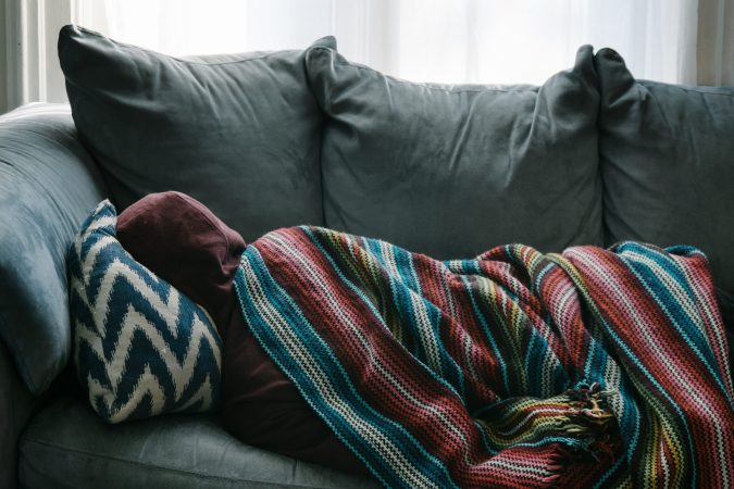 person lying on couch with blanket over them