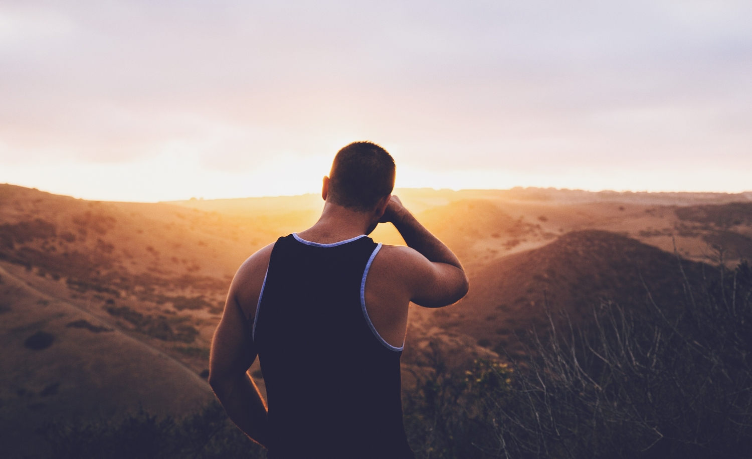 a person standing in the wilderness rubbing their face as the sun sets