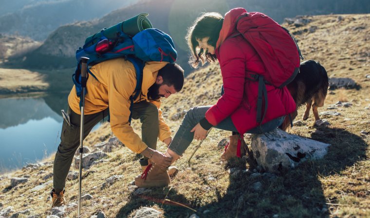 A woman has sprained her ankle while hiking, her friend uses the first aid kit to tend to the injury