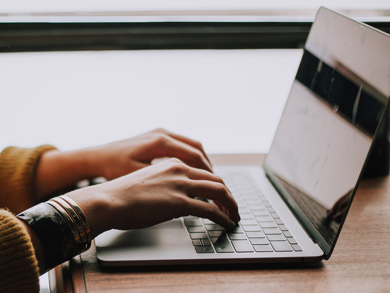 hands on a gray laptop on a wooden table or desk