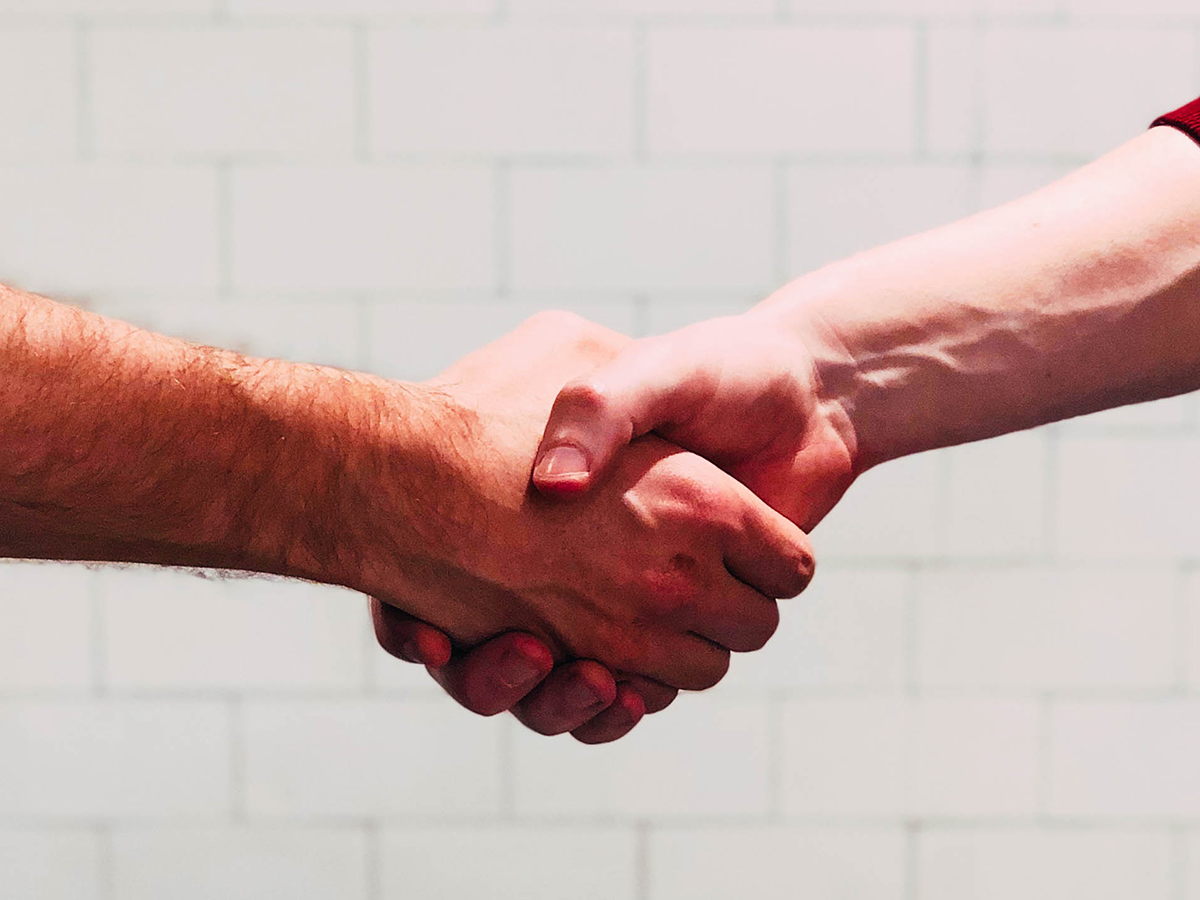 two people shaking hands in front of a white wall