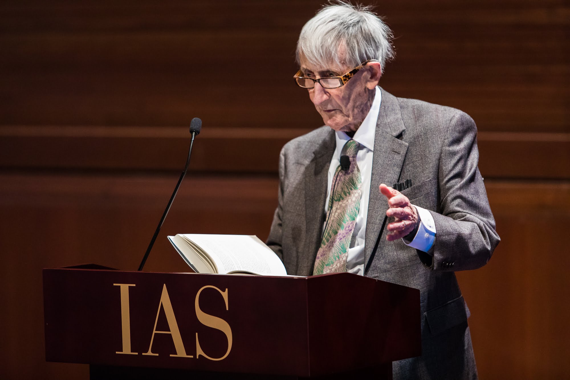 An old man at a podium reading from a book