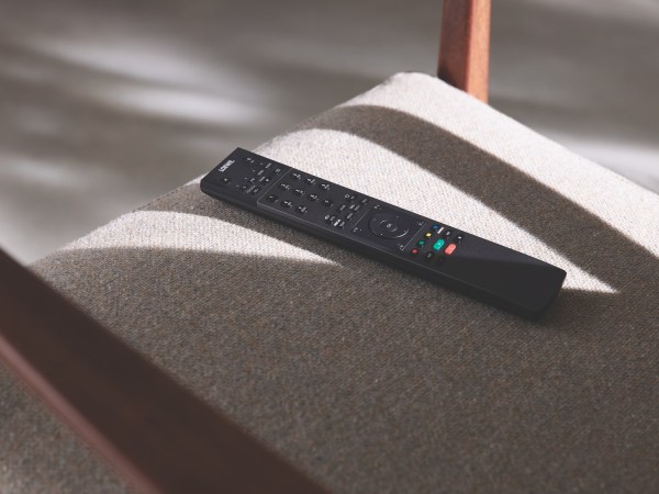 A black TV remote on a gray chair in some sunlight.
