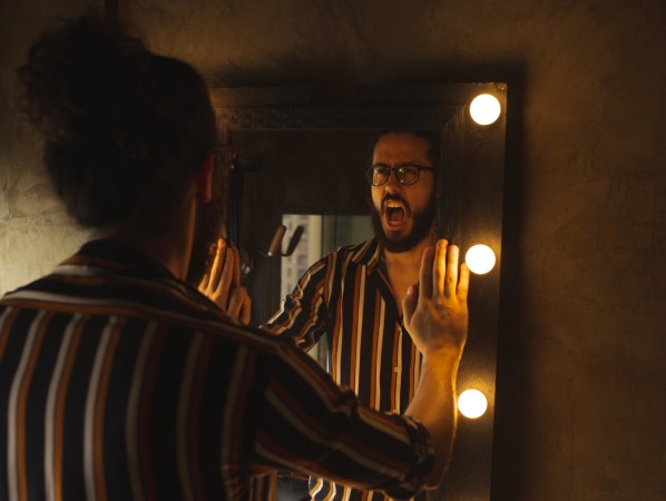 A man standing at a mirror and yelling at his reflection in the dark.