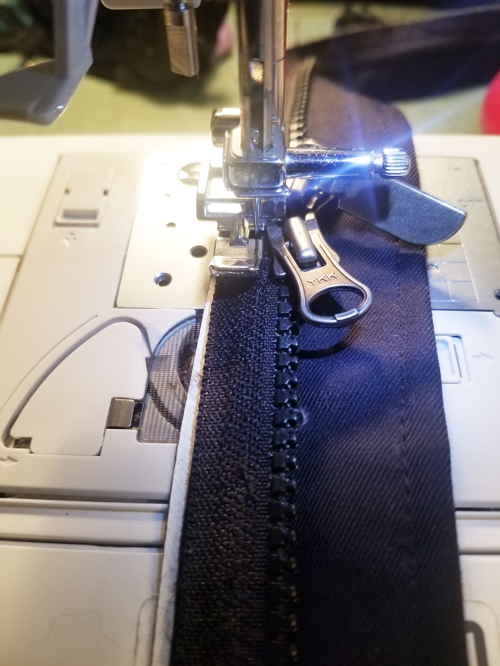 a person sewing a replacement zipper onto a winter jacket, using a sewing machine