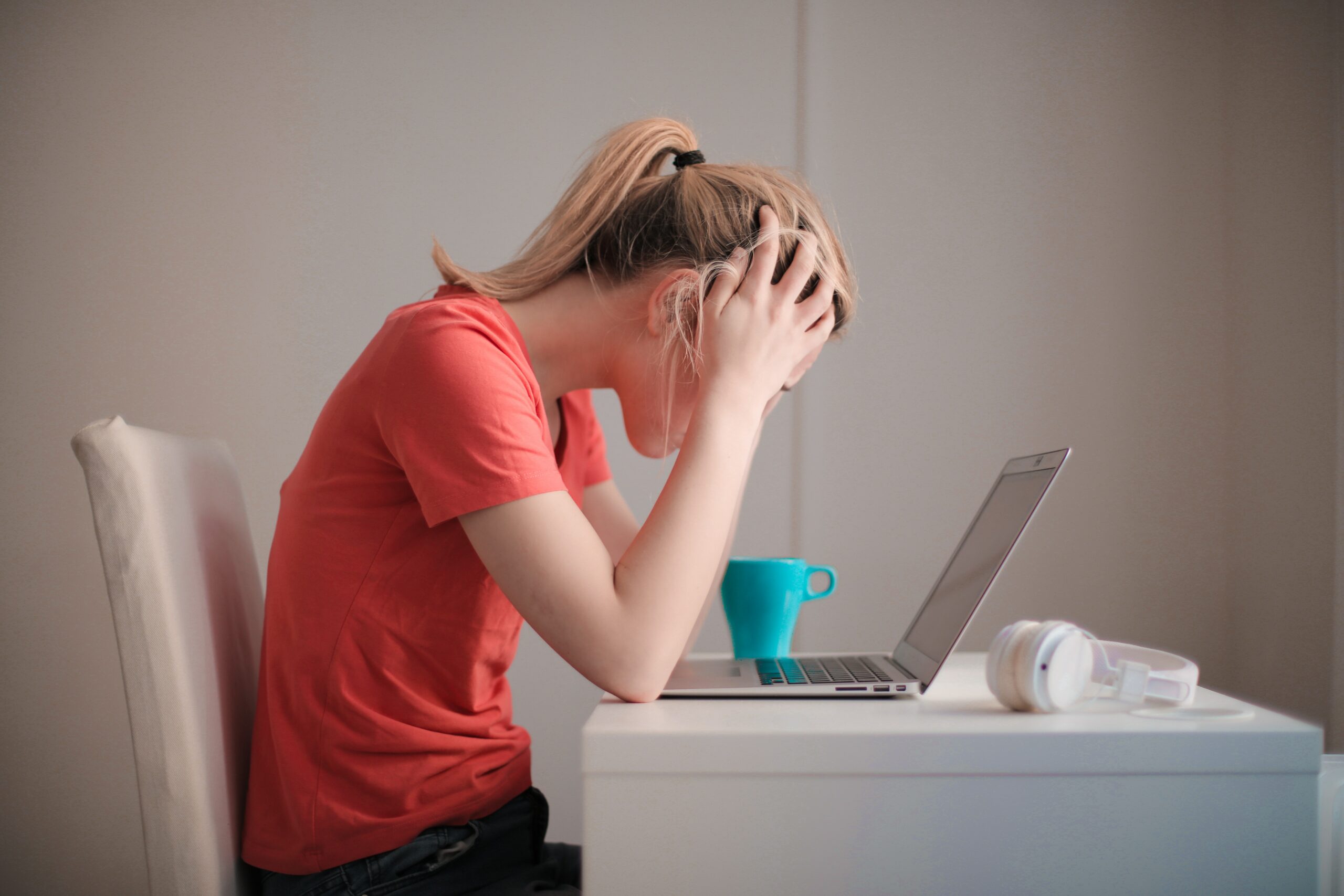 A woman in red with her head in her hands in front of a laptop