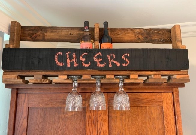 a wall-mounted wine rack made out of a reclaimed wood pallet, with a chalkboard and a wine glass holder