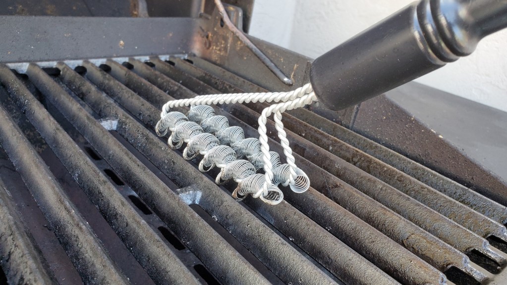 a person brushing a grill grate with a bristle-less wire brush