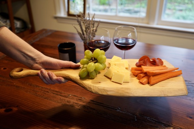 a person holding a handmade DIY cutting board with cheese, grapes, carrots, and strawberries on it