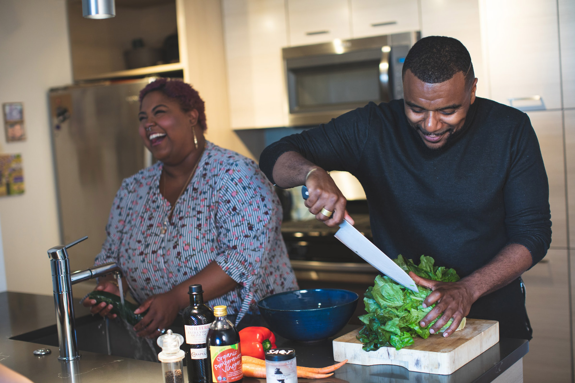 Black man and woman couple cooking with salad ingredients in kitchen