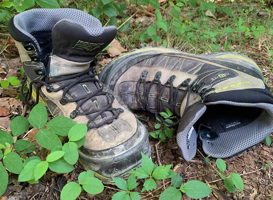 A pair of boots in the dirt and grass.