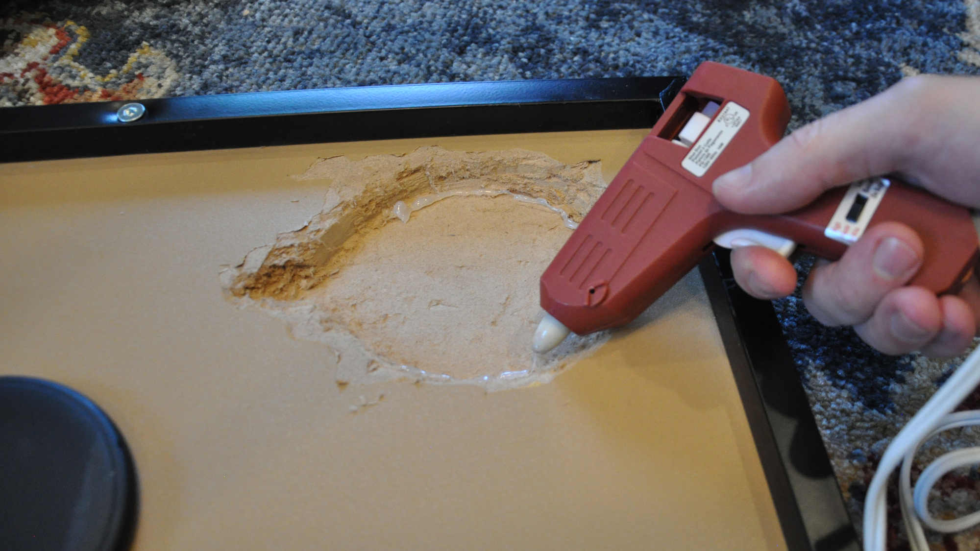 a person applying hot glue to the underside of a table for a wireless charging pad