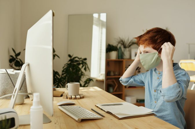 Boy doing online school in a mask.