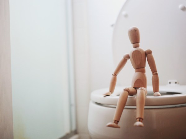 a wooden doll sitting on a toilet