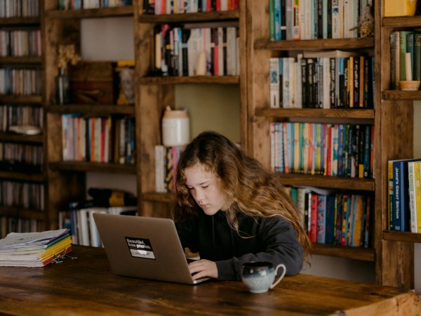 a child student using an Apple mac laptop for school work on a wooden table