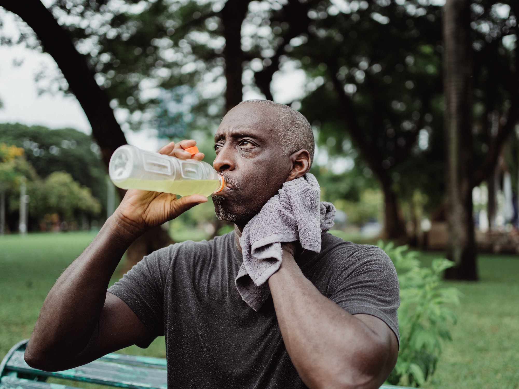 man drinking sports drink sweating sitting on bench