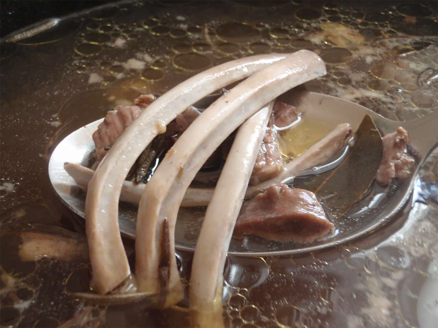 A large pot of chicken or beef bone broth with bits of bones, herbs and meat floating in the broth.