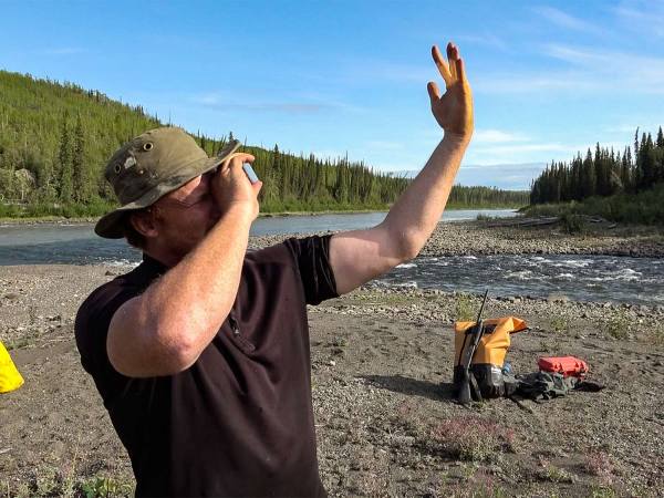 A man holds a survival mirror to his face to reflect on his other hand.