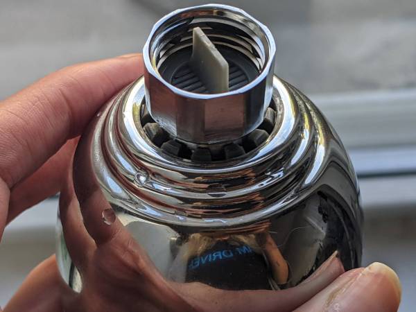 A person holding a shiny, clean showerhead, and you can see their reflection in it.