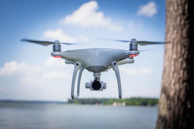 a drone hovers next to a lake and a tree