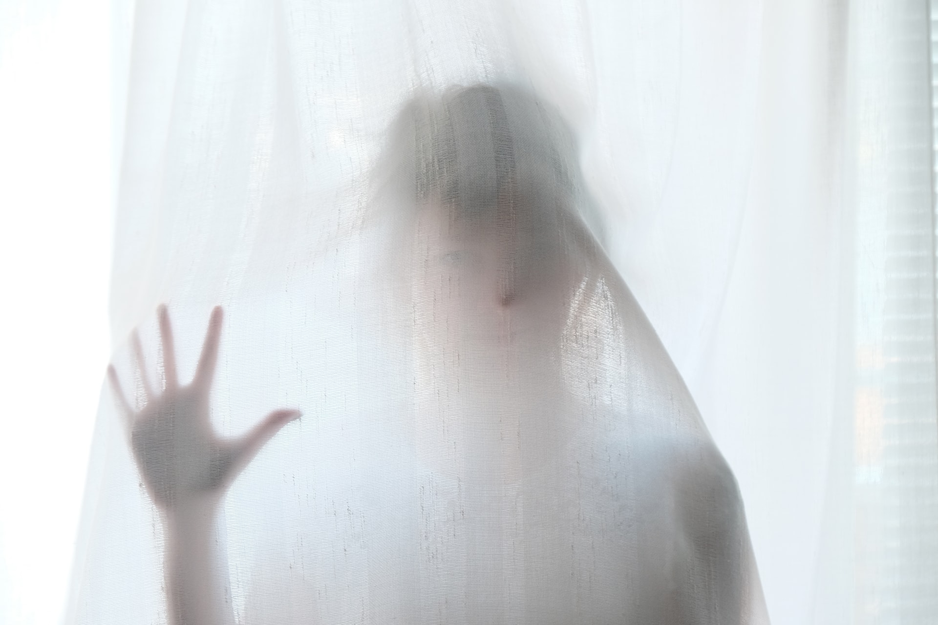 A person stands behind a white gauzy curtain in a spooky fashion