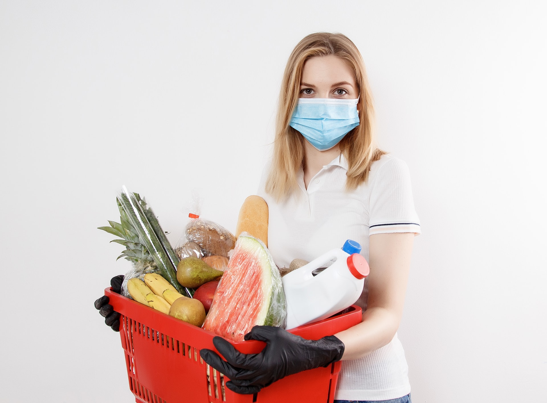 Person in a mask and disposable gloves holding a basket of groceries