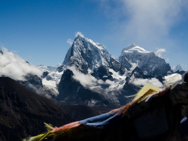 A photo of Mount Everest behind clouds and under a blue sky.