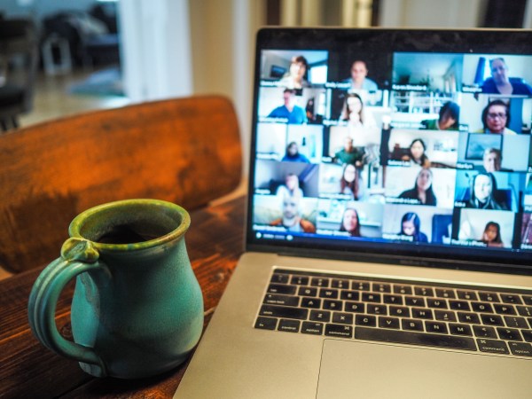 A mug of coffee or tea next to a Macbook laptop with Zoom open and full of people.