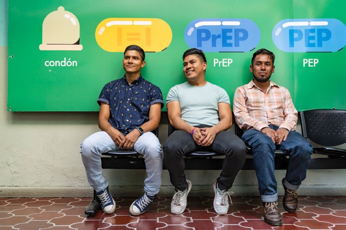 Three staff members sit at a free HIV clinic in Guatemala City with green PrEP banners in the back