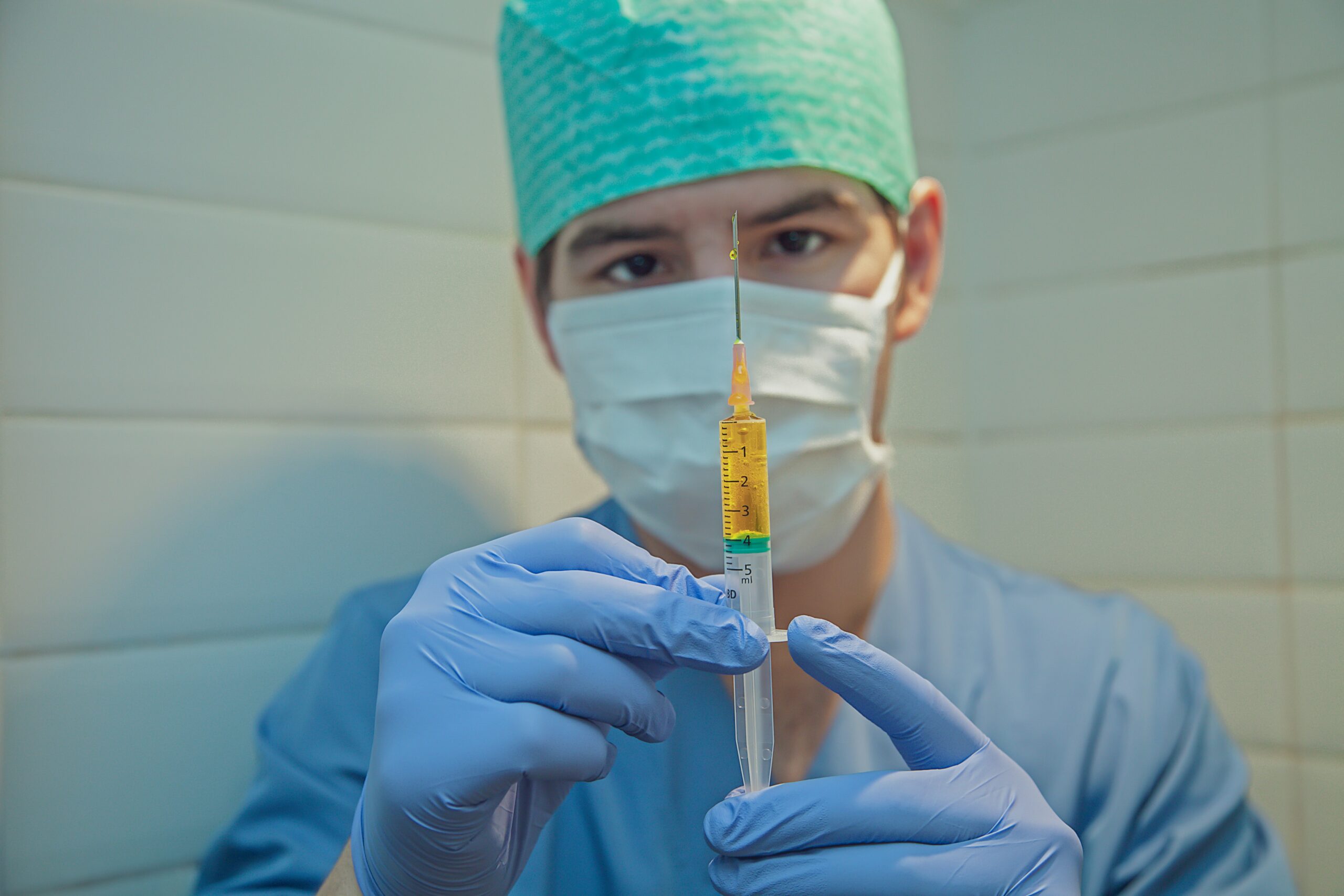 A man in medical PPE holds a syringe full of yellow liquid