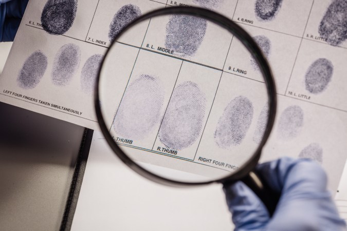 A gloved hand holding a magnifying glass and looking at fingerprints