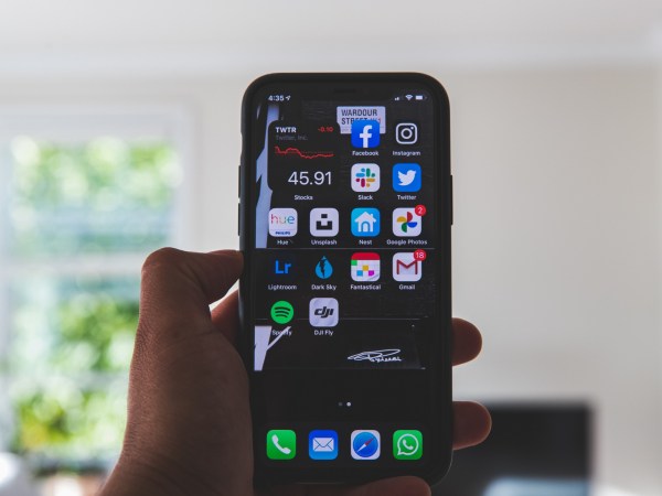 A person holding a smartphone in front of them inside a white room in a house.